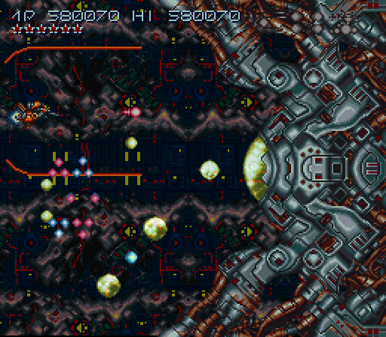 Na imagem, Axelay. Jogo shoot'em up do Super Nintendo. No lado esquerdo há uma pequena nave que é controlada pelo jogador enquanto na direita está o último chefão, um nave gigante que parece com grande polvo metálico com um olho de vidro no meio