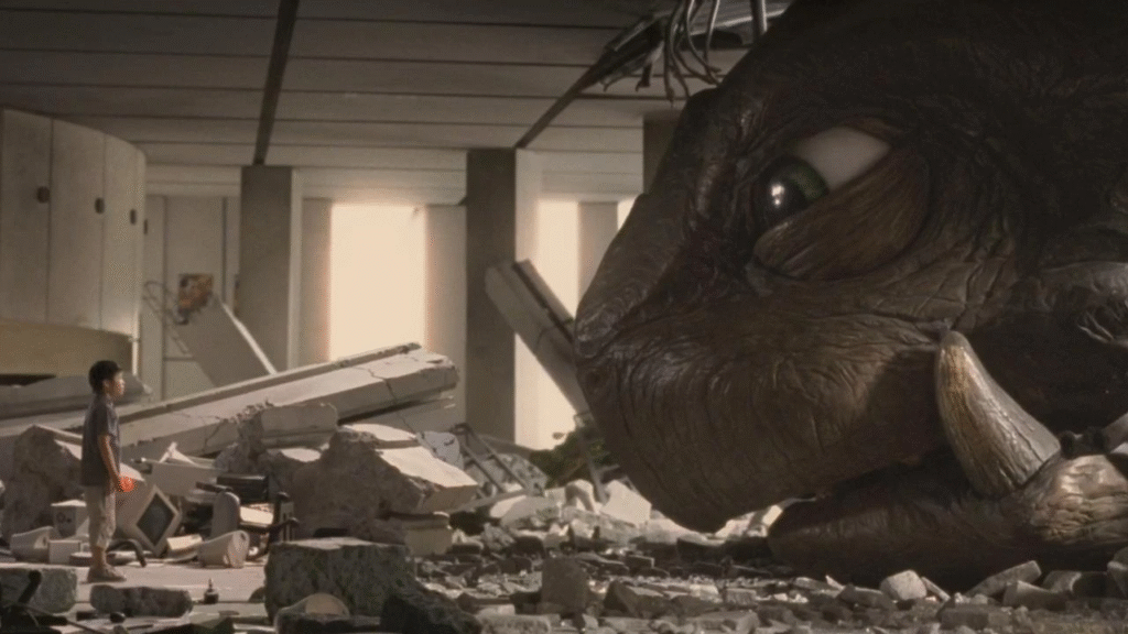 Cena de Gamera the Brave. O garoto Toru segura uma rocha vermelha e encara Toto, o Gamera crescido, que está com a sua cabeça presa num prédio
