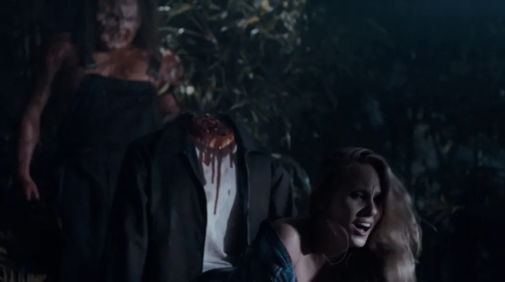 Cena do filme Terror no Pântano 2. Uma mulher está de quatro com seu amante atrás dela e o vilão do filme, Victor Crowler, os observa no fundo da tela depois de cortar a cabeça do homem com sua machadinha