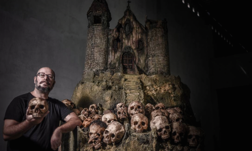 Foto de Rodrigo Aragão, um dos grandes nome do terror nacional, ao lado de uma miniatura de uma igreja antiga usada no seu filme O Cemitério das Almas Perdidas