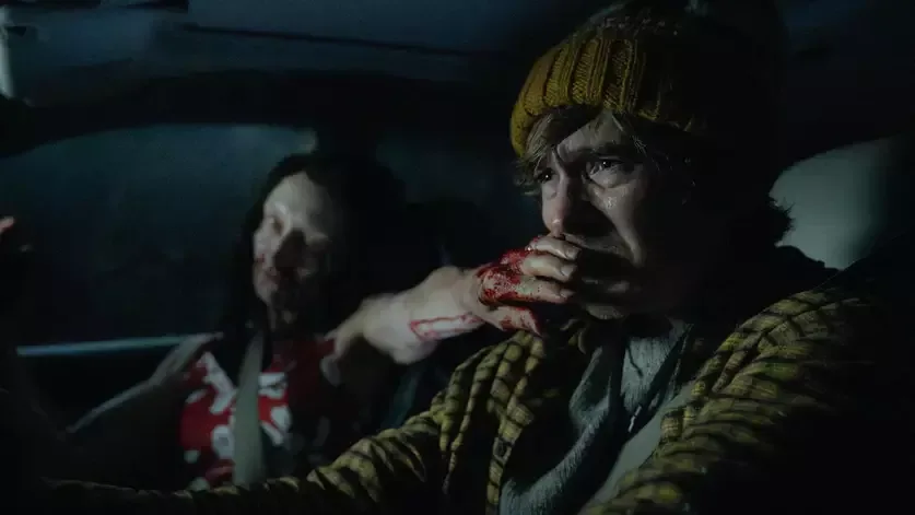 Cena do filme Resident Evil (2026), do diretor Zach Cregger, mostrando o protagonista Bryan levando uma mulher infectada no seu carro
